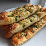 A stack of golden brown, soft breadsticks topped generously with garlic butter and fresh parsley.