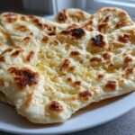 Close-up of several pieces of soft naan bread, slightly charred and glistening with melted butter.