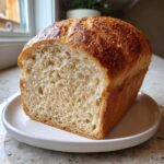 A freshly baked loaf of soft whole wheat bread, sliced to show the airy interior crumb, resting on a white plate.