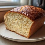 A freshly baked loaf of soft whole wheat bread, sliced to show the light, airy crumb and shiny golden-brown crust.