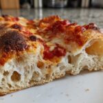 Close-up of a slice of pizza showing the airy, open crumb structure achieved with sourdough discard pizza dough.