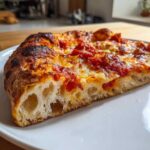 Close-up of a slice of pizza showing the airy, open crumb structure of the sourdough discard pizza dough crust.