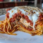 A thick, square slice of baked spaghetti pie with layers of pasta, meat sauce, ricotta, and melted mozzarella cheese on top.