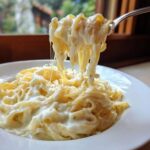 A fork lifting fettuccine noodles coated in rich, creamy homemade alfredo sauce, showing cheese stretch.