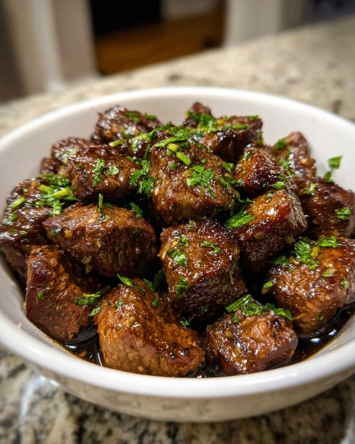 Close-up of tender, glazed crockpot steak bites served in a white bowl and sprinkled with fresh parsley.