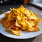 A mound of tortilla chips completely smothered in thick, bright yellow homemade nacho cheese sauce on a white plate.