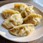 Five perfectly pleated Traditional Chinese Dumplings, glistening from steaming, served on a white plate.