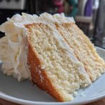 Close-up of a moist slice of vanilla cake recipe layered with thick white buttercream frosting.
