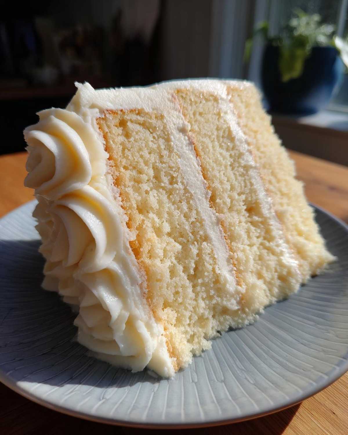 A tall slice of moist vanilla cake recipe with three layers and thick white buttercream frosting.
