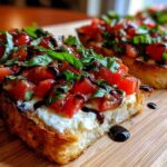 Close-up of toasted bread topped with cheese, diced tomatoes, basil, and balsamic glaze, resembling a bruschetta dip serving.