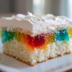 Close-up of a moist slice of 3-color jello poke cake showing colorful gelatin pockets and white whipped topping.