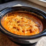 Close-up of bubbling, cheesy chili cheese dip with melted white cheese swirls in a black slow cooker.