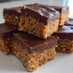Stack of delicious, chewy homemade protein bars topped with a thick layer of melted chocolate.