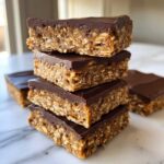 A stack of four homemade protein bars made with oats and topped with a smooth layer of dark chocolate.