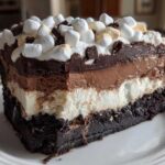 A thick slice of 5-layer mud pie showing distinct layers of dark crust, white filling, chocolate mousse, and topped with whipped cream and marshmallows.