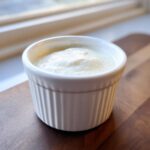 A small white ramekin filled with creamy, white horseradish sauce, sitting on a wooden board.