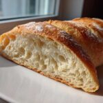 Close-up of a freshly baked french bread loaf, sliced to show the open, airy interior crumb and golden crust.