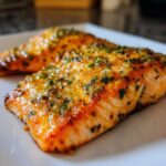 Close-up of two glistening, golden-brown air fryer salmon fillets topped with herbs and garlic.
