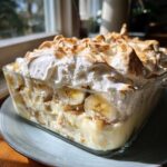 A close-up of homemade banana pudding in a glass dish, featuring layers of pudding, bananas, and toasted meringue.