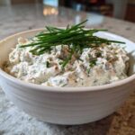 A white bowl filled with creamy blue cheese dip, garnished generously with fresh green chives.
