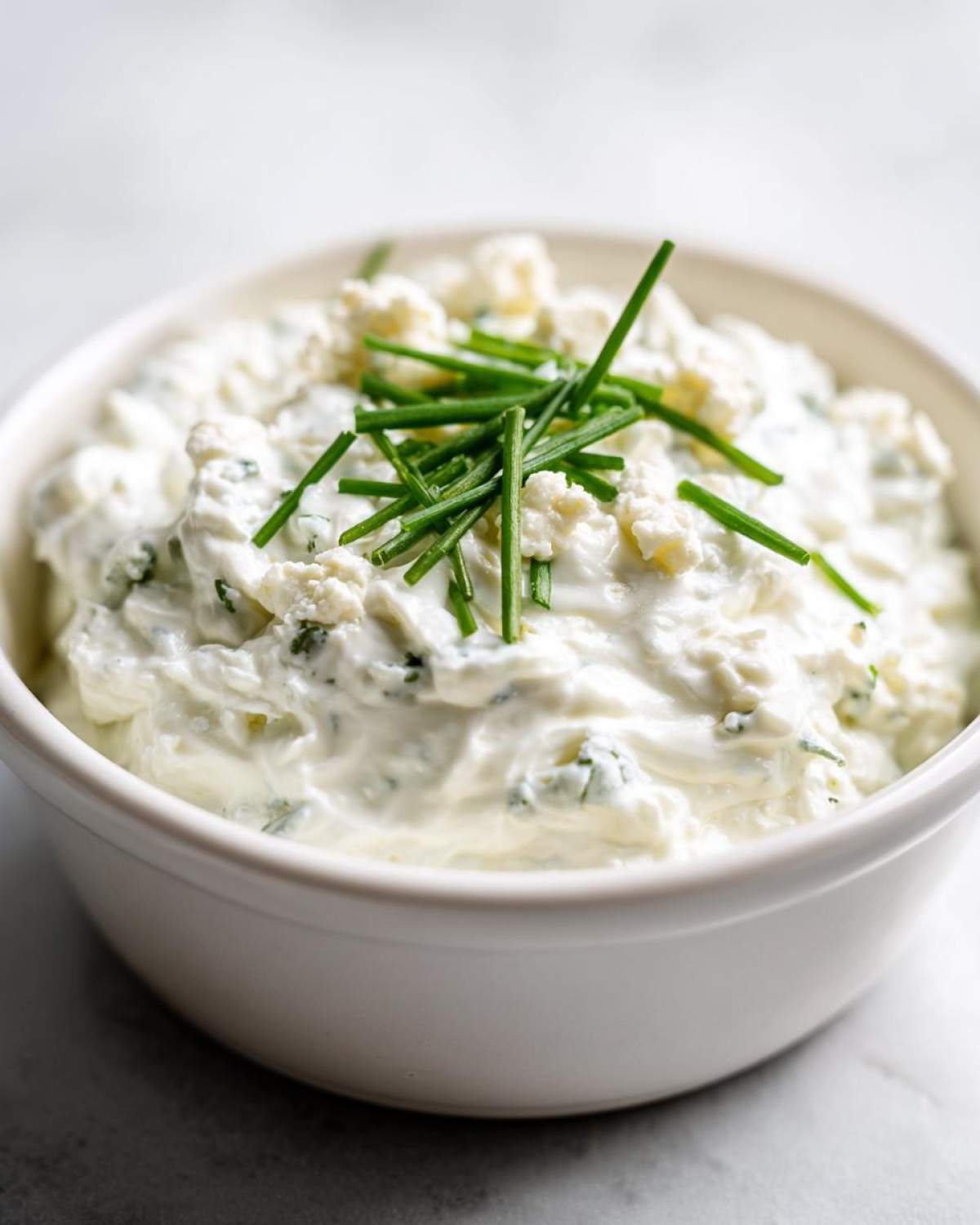 A white bowl filled with creamy blue cheese dip, topped with crumbled blue cheese and fresh chives.