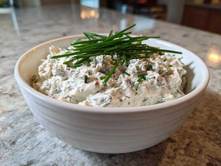 A white bowl filled with creamy blue cheese dip, garnished generously with fresh green chives.