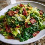 Close-up of a delicious cabbage recipe featuring wilted green cabbage mixed with crispy, crumbled bacon pieces served on a white plate.