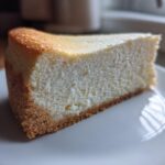 A close-up, featured image of a thick slice of creamy baked cheesecake recipe on a white plate.