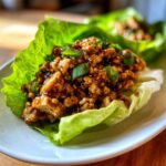 Close-up of a savory, saucy chicken lettuce wraps filling served in a crisp butter lettuce cup, garnished with green onions.
