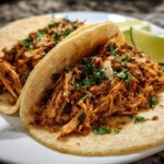 Two delicious chicken tacos filled with shredded seasoned chicken, topped with cilantro and onion, served with lime wedges.