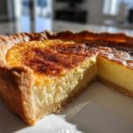 Close-up of a rich, creamy custard pie with a browned, spiced top and a thick crust, with one slice removed.