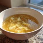 A white bowl filled with golden broth and delicate ribbons of cooked egg in this amazing egg drop soup.