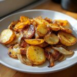 A close-up of perfectly golden brown fried potatoes mixed with caramelized onions on a white plate.