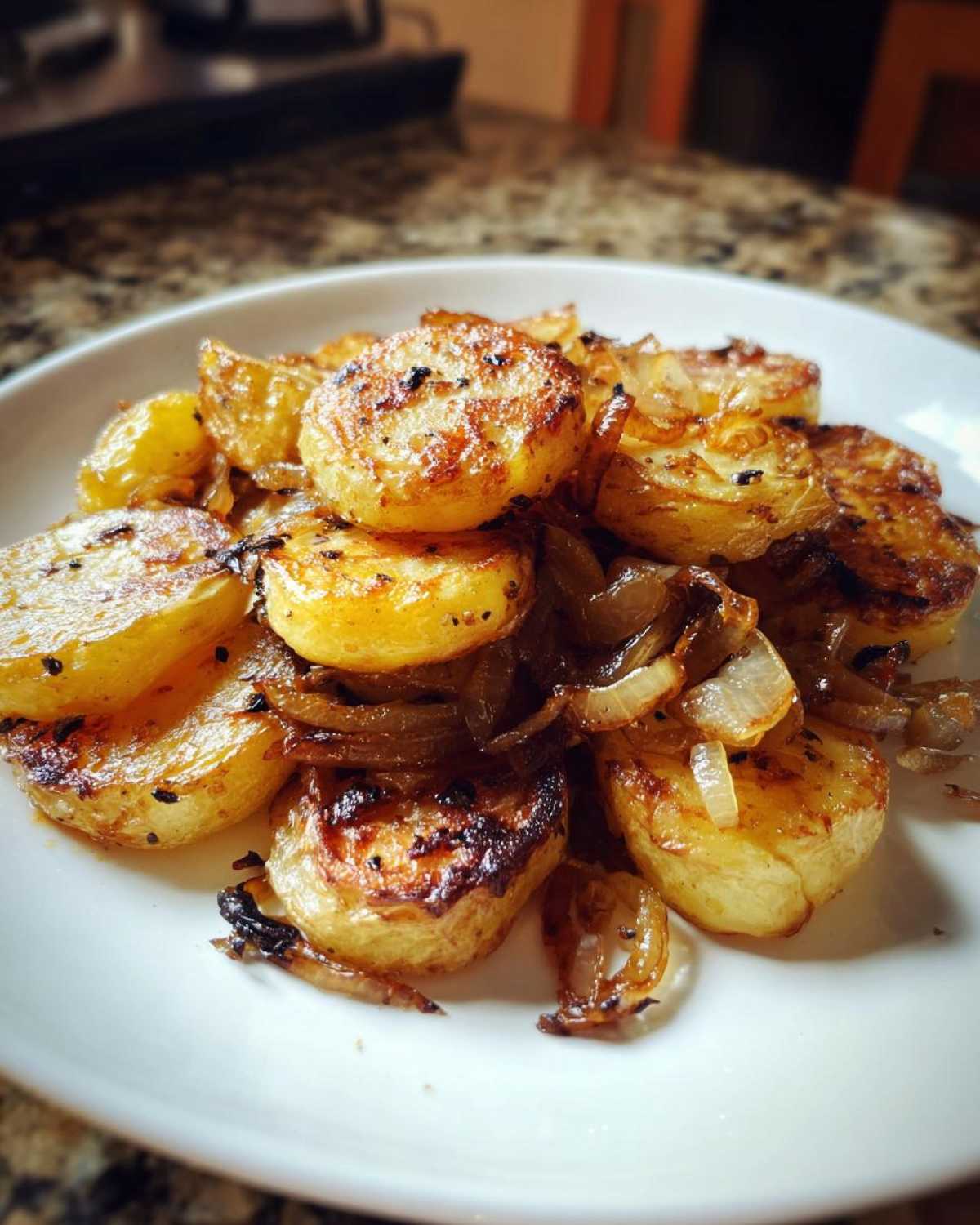 A close-up of perfectly golden brown sliced fried potatoes mixed with caramelized onions served on a white plate.