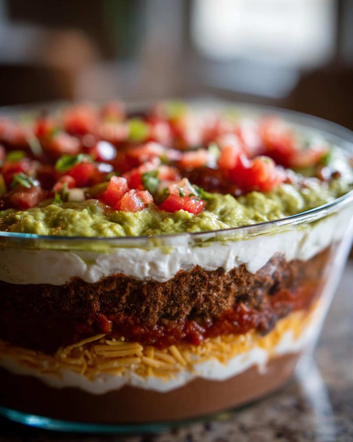 Close-up of a beautiful 7 layer dip showing distinct layers of beans, cheese, sour cream, guacamole, and tomatoes.
