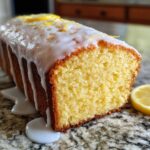 Close-up of a moist lemon pound cake loaf, drizzled with thick white glaze and topped with zest.