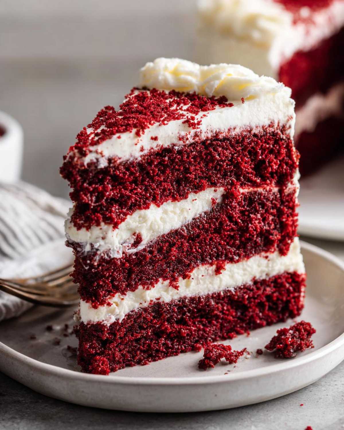 Close-up of a tall slice of moist red velvet cake with three layers and thick cream cheese frosting.