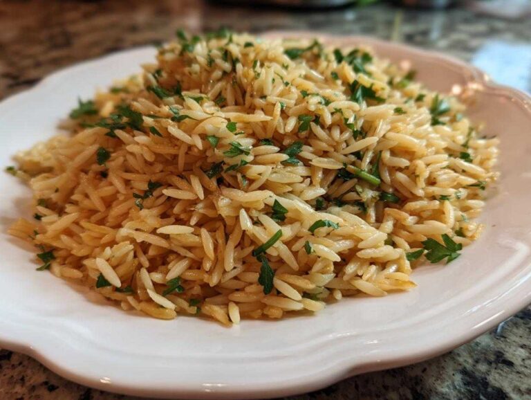 Close-up of a serving of fluffy, golden rice pilaf garnished with chopped fresh parsley on a white plate.