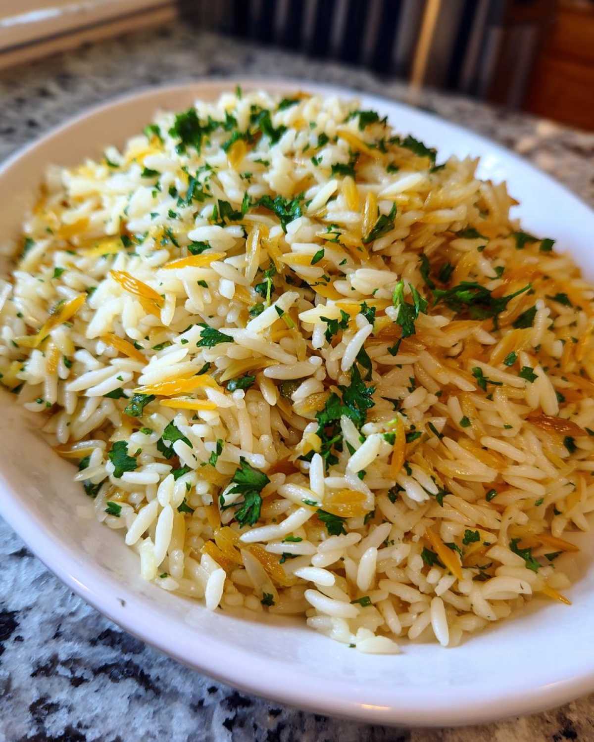 Close-up of a white bowl filled with fluffy rice pilaf mixed with toasted vermicelli and topped with fresh chopped parsley.