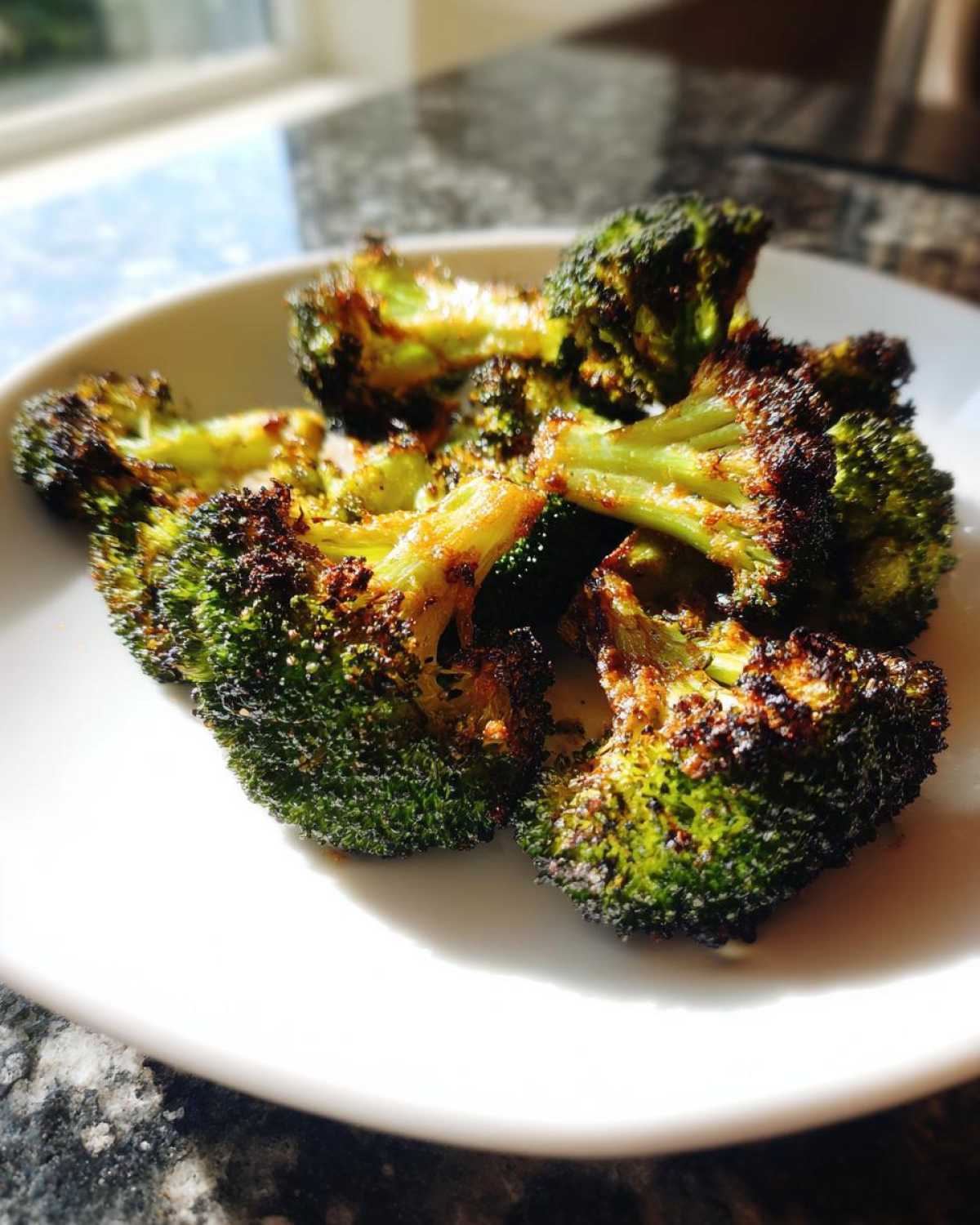 Close-up of perfectly roasted broccoli florets with crispy, browned edges served on a white plate.