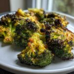 Close-up of perfectly seasoned and charred roasted broccoli on a white plate.