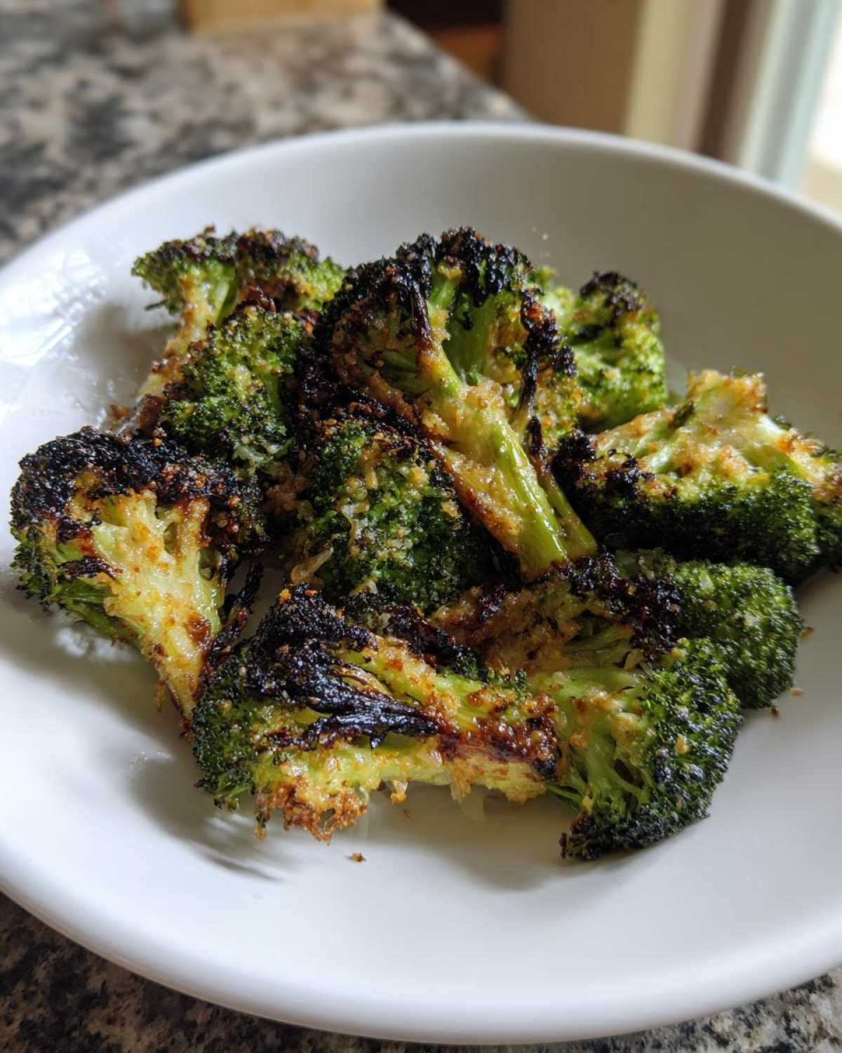 Close-up of perfectly charred and seasoned roasted broccoli florets served in a white bowl.