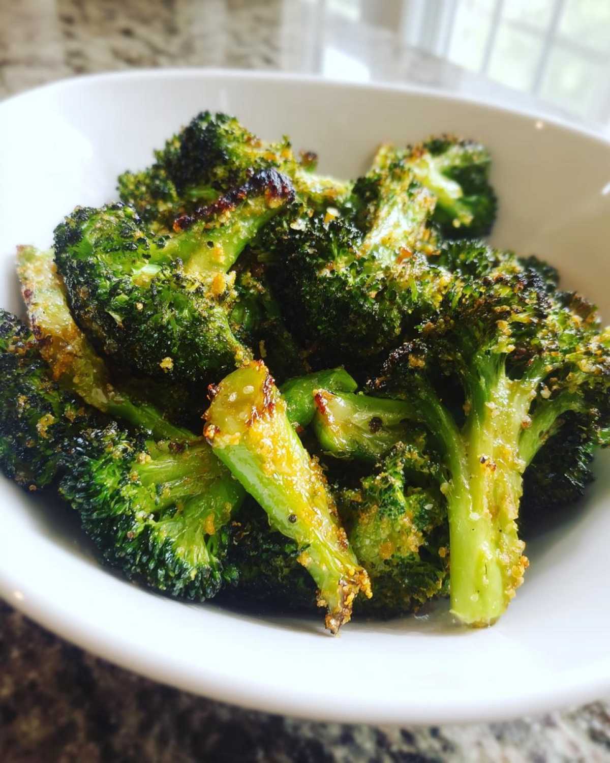Close-up of bright green, crispy roasted broccoli florets coated in seasoning, served in a white bowl.