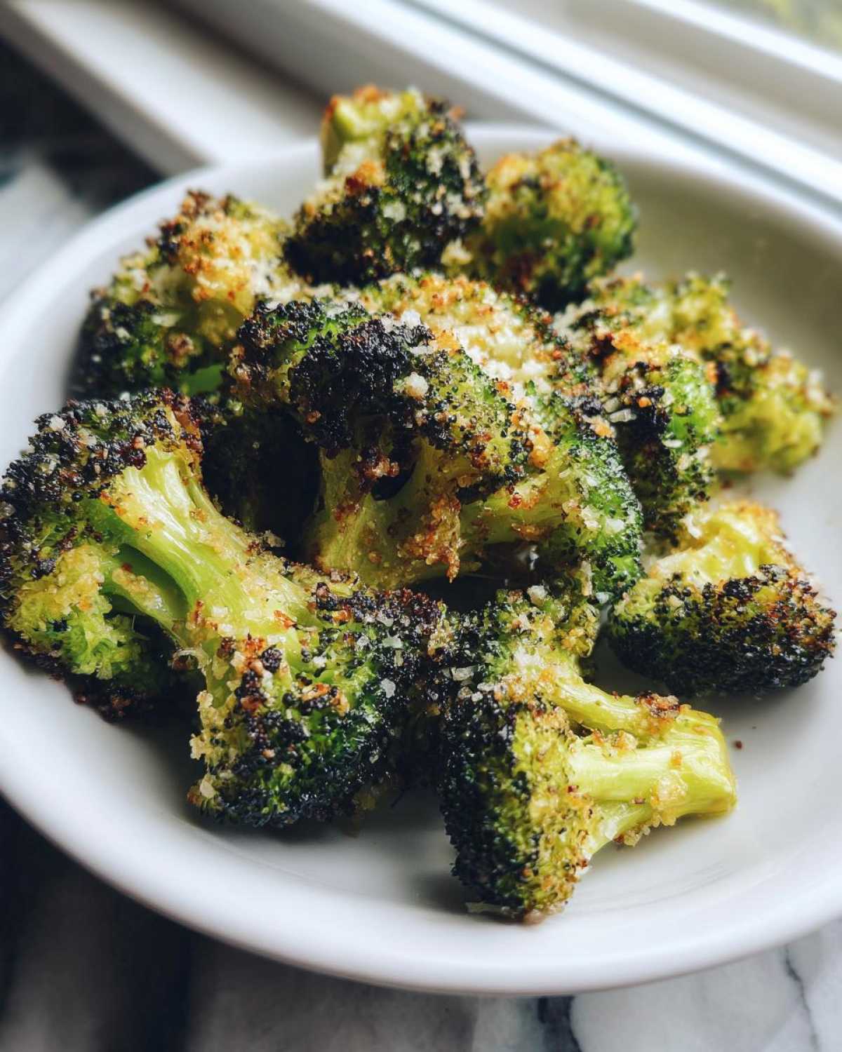 Close-up of bright green roasted broccoli florets topped with crispy breadcrumbs and Parmesan cheese.