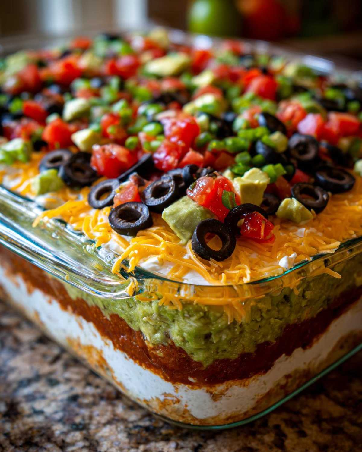 Close-up view showing the distinct layers of the Amazing Seven layer dip, topped with cheese, olives, tomatoes, and avocado.