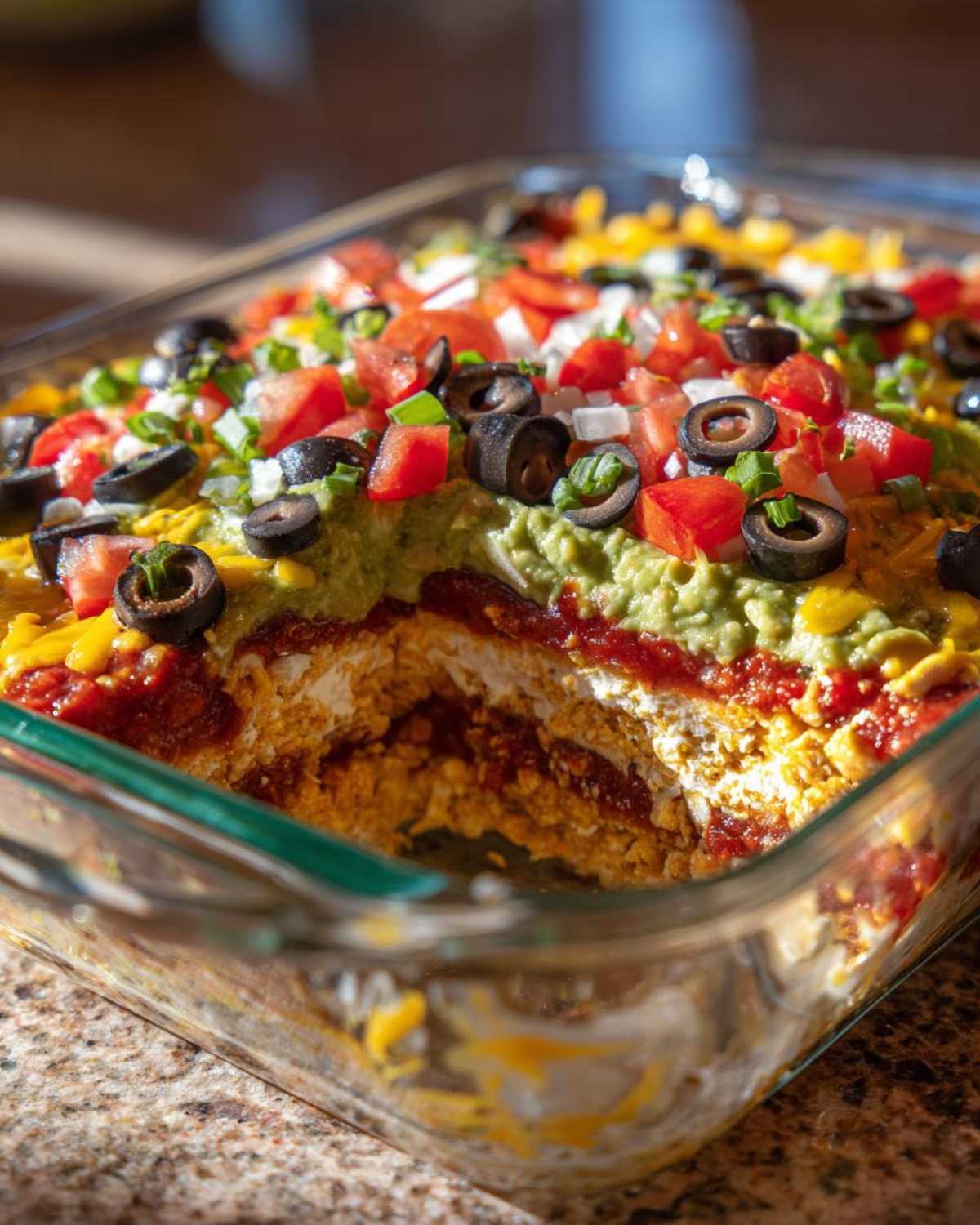 Close-up of Amazing Seven layer dip in a glass dish with a portion scooped out, showing layers of toppings.