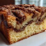 Close-up of a moist slice of sour cream coffee cake showing the yellow cake, cinnamon swirl, and crunchy streusel topping.