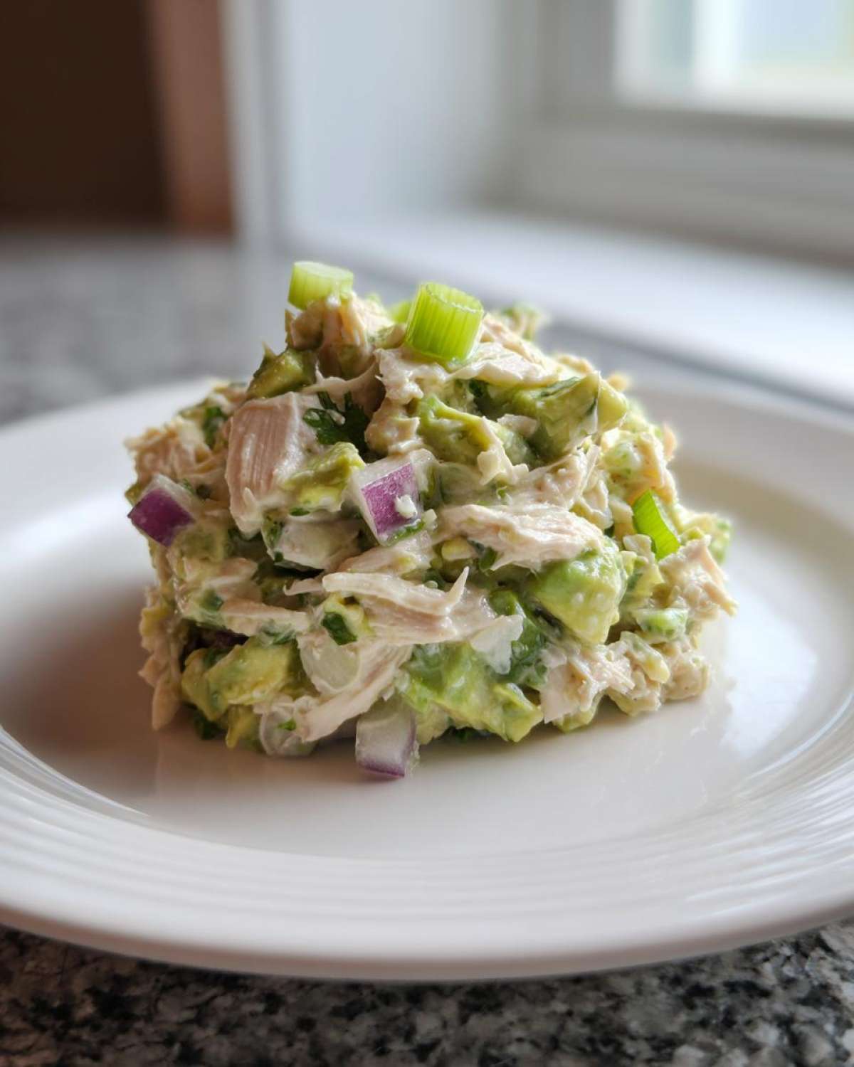 A scoop of creamy avocado chicken salad mixed with red onion and topped with green onion slices.