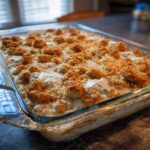 A creamy, baked hot chicken salad casserole topped with golden brown crunchy crumbs in a clear glass baking dish.