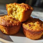 Three golden-brown banana protein muffins stacked on a plate, one broken open to show the moist interior texture.